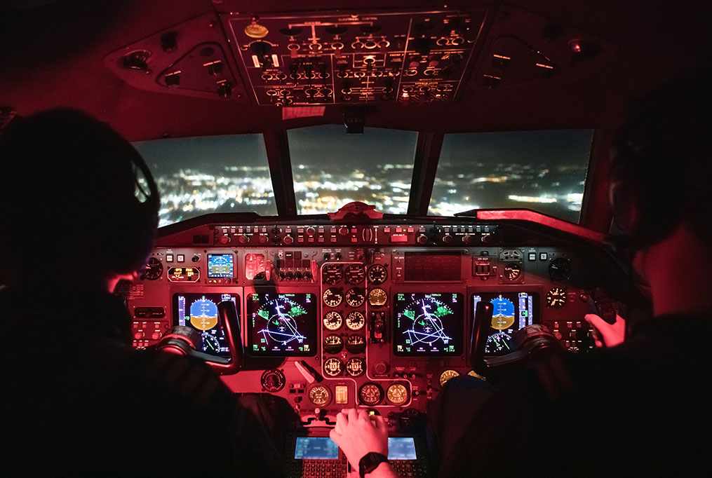 night time interior photo of aircraft cockpit with pilots